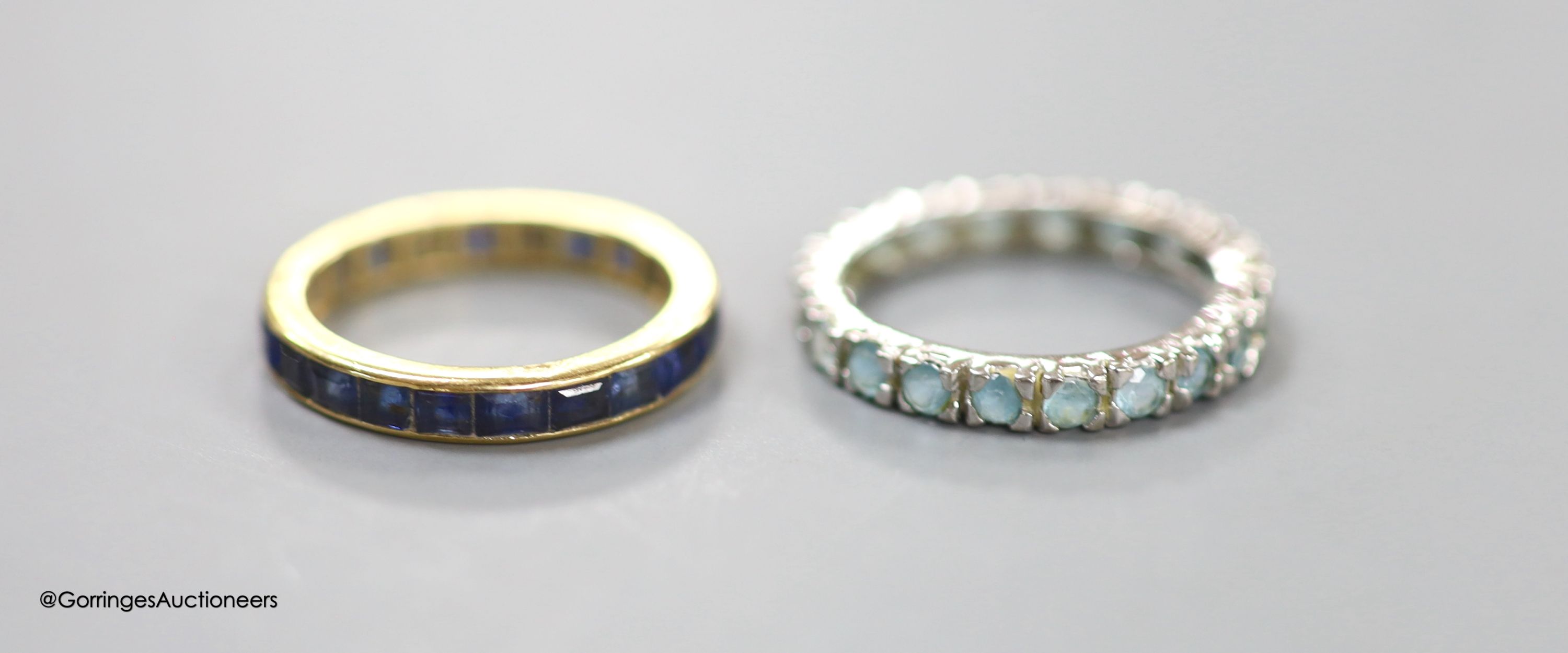 A yellow metal and sapphire set full eternity ring, size M, gross weight 2.8 grams and a white metal and blue gem set full eternity ring, size N/O, gross 2.4 grams.